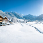 Drohnenaufnahme aus der Luft im Winter mit Schnee bei Kaiserwetter mit Blauem Himmel und einer Ferienwohnung in den Bergen