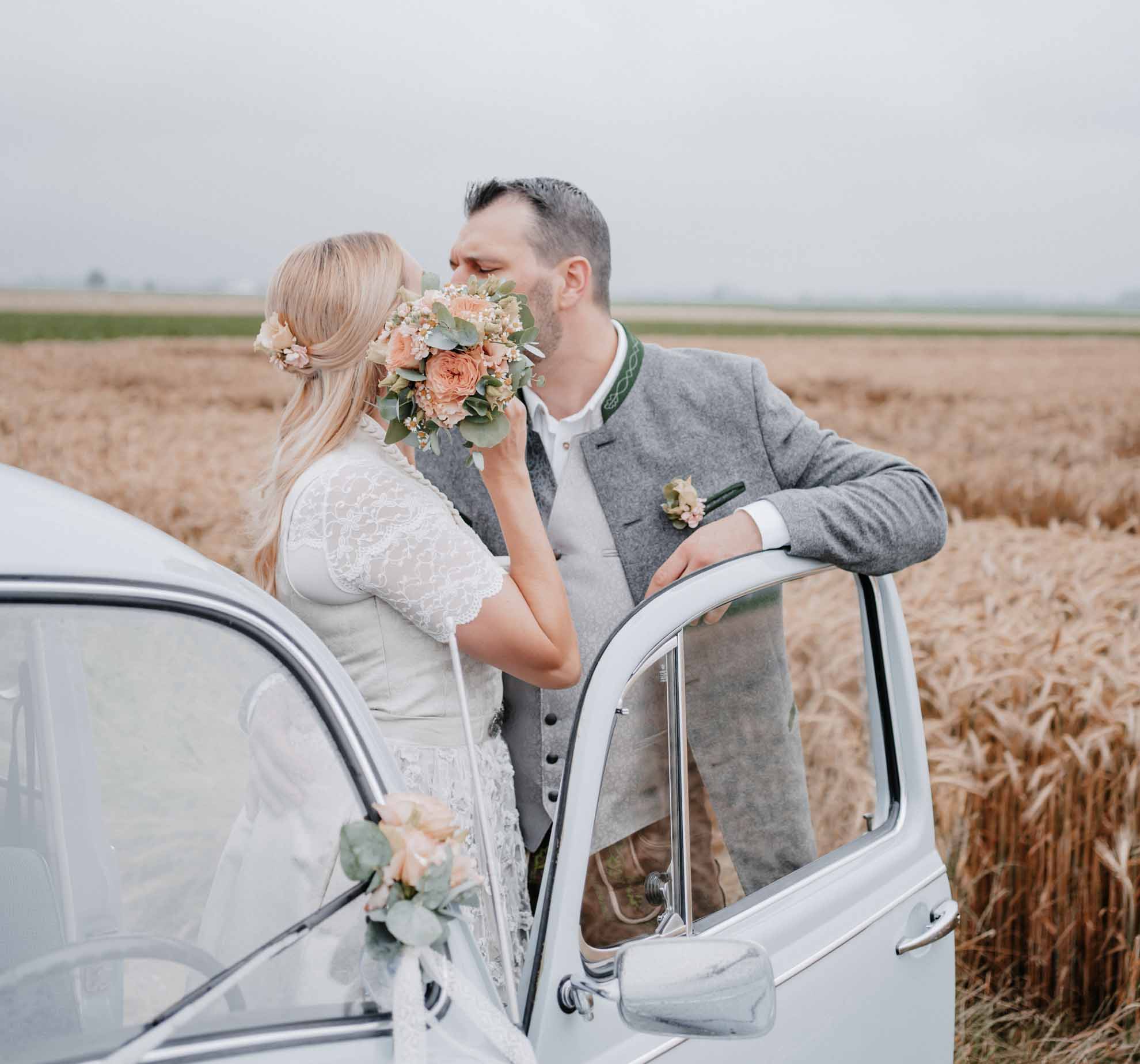 Hochzeitsfoto eines Brautpaares im an einem VW Käfer Küssend