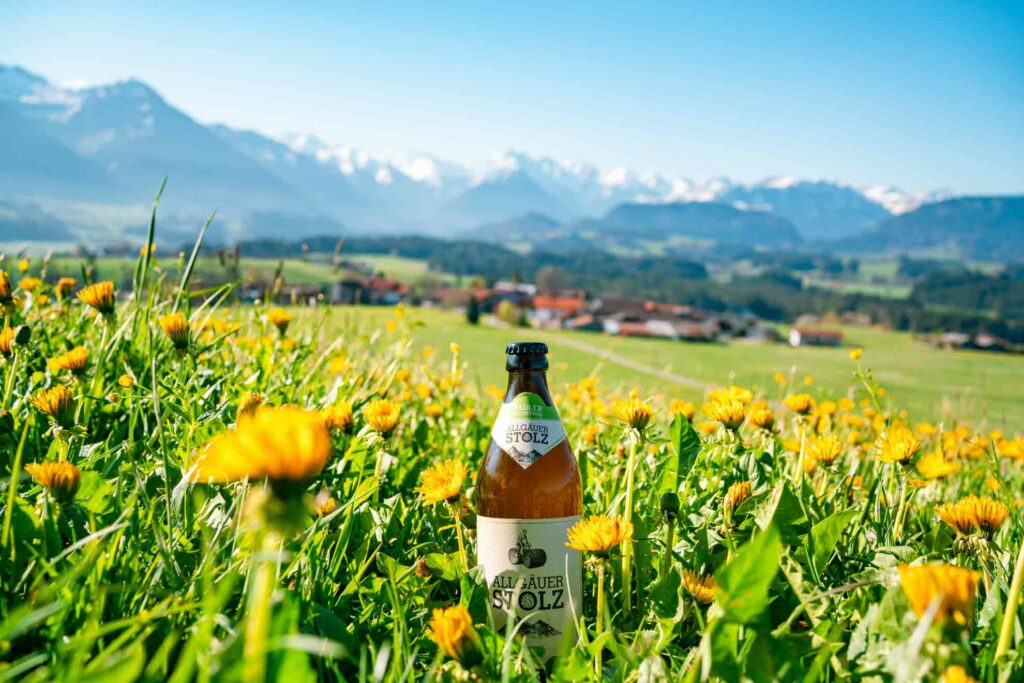 Produktfoto Bier einer Privatbrauerei im Frühling mit Löwenzahn und den Allgäuer Alpen im Hintergrund