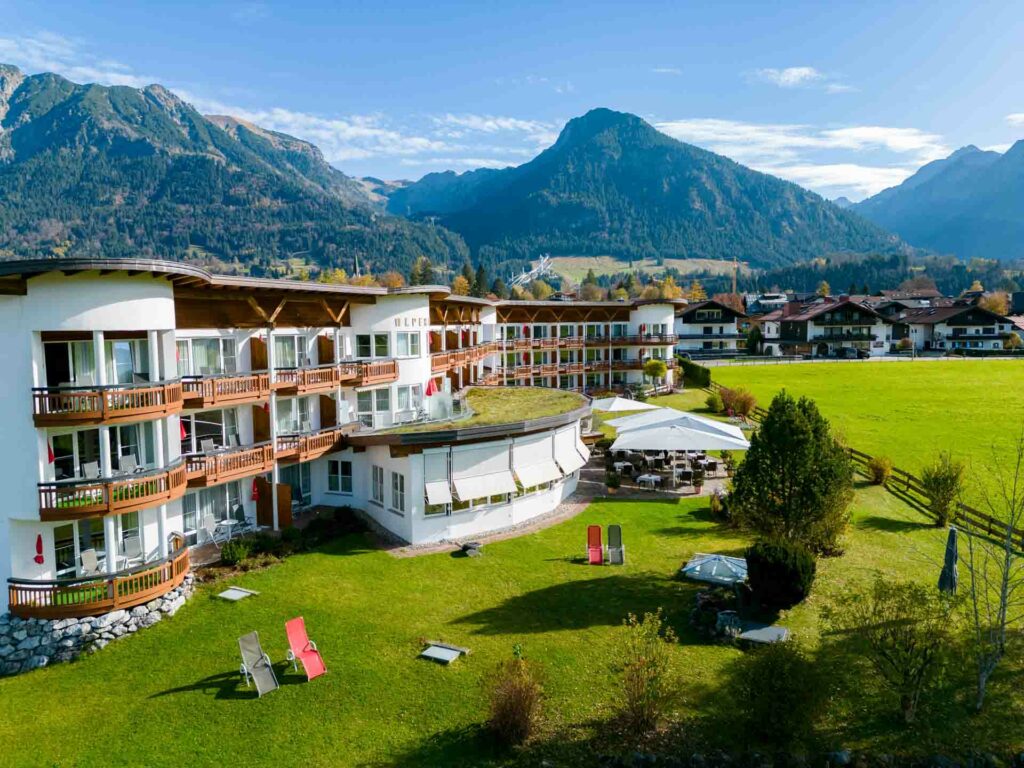 Hotel in Oberstdorf mit der Nebelhornbahn im Hintergrund und grüner Wiese