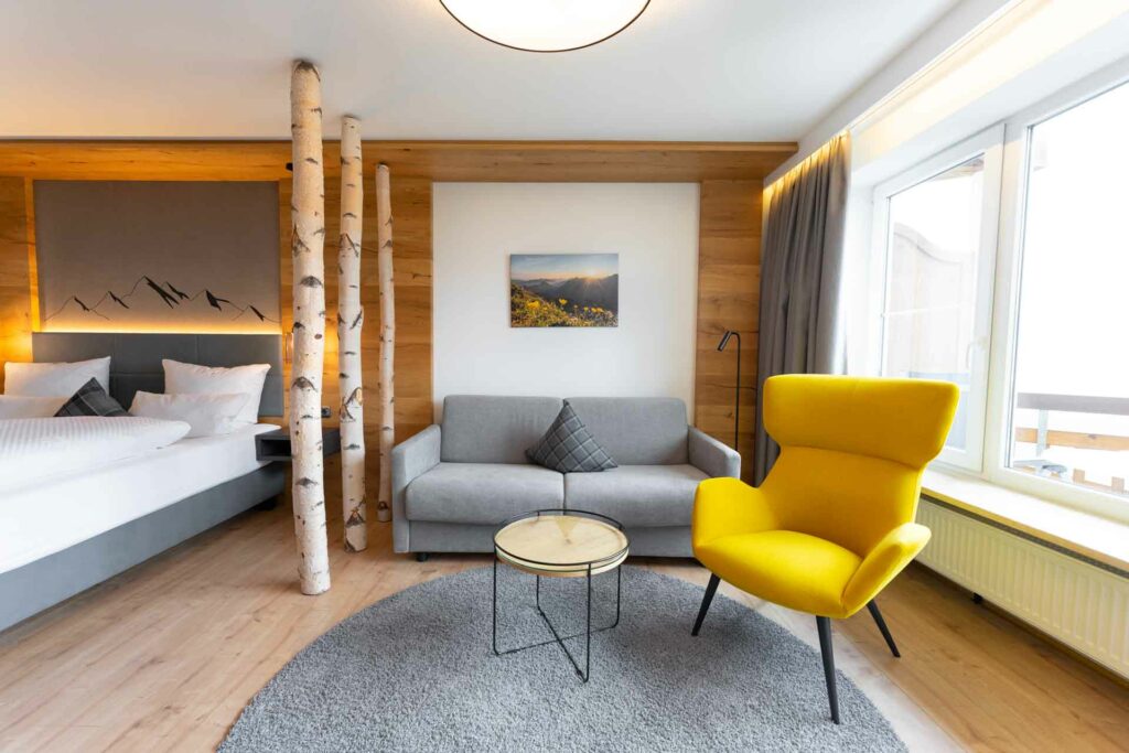 Einzelzimmer mit Bett, Couch und gelbem Sessel im Hotel