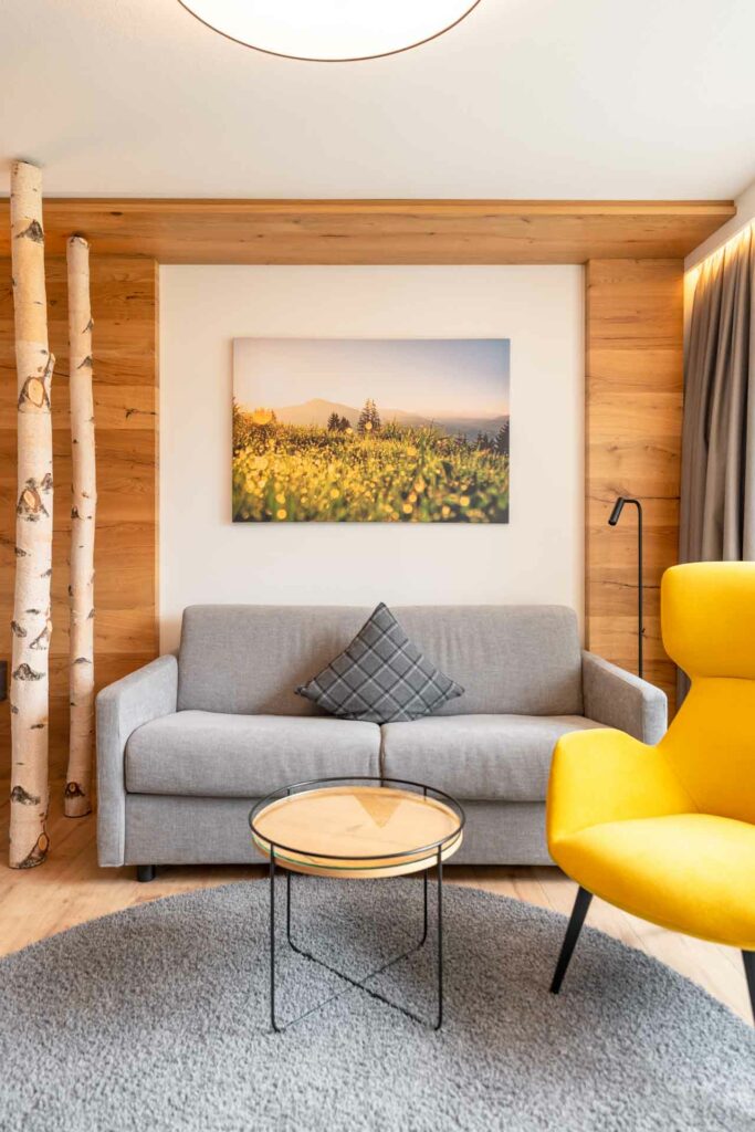 Wohnzimmer mit grauer Couch, gelbem Sessel links, Birkenstöcke links und Leinwand an der Wand